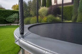 Trampoline met veiligheidsnet en randkussen in een tuin, klaar voor onderhoud