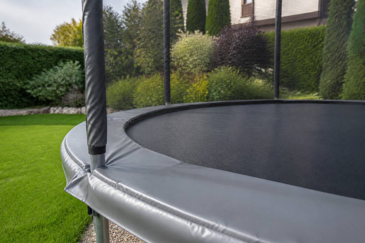 Trampoline met veiligheidsnet en randkussen in een tuin, klaar voor onderhoud